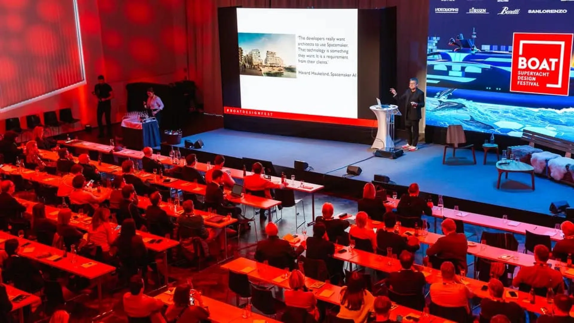 Konferenzszene mit Publikum und Präsentation auf der Bühne